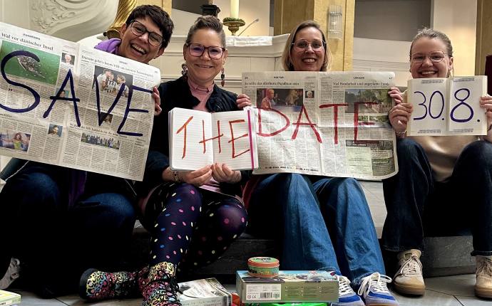 Jenny, Meike, Nele und Gesa halten Zeitung, Heft, Buch hoch mit dem Text "Safe the date, 30.8." Vor ihnen sind Spiele, Bücher, Stifte Jenny, Meike, Nele und Gesa halten Zeitung, Heft, Buch hoch mit dem Text "Safe the date, 30.8." Vor ihnen sind Spiele, Bücher, Stifte
