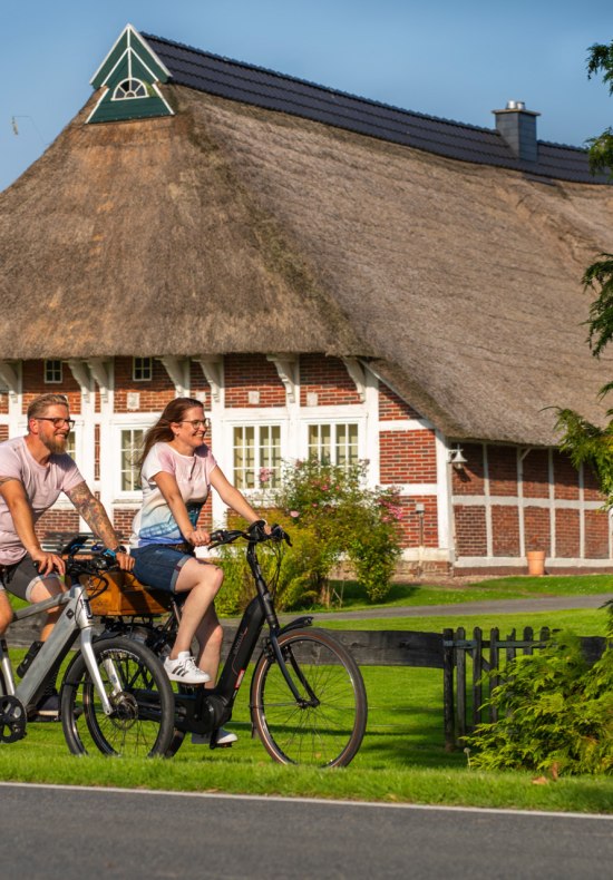 Radfahrer auf der Route um Oldenburg vor einem Reetdachhaus in Wesermarsch