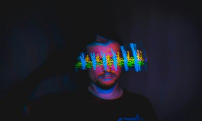 Ein Mann im dunkeln. Vor seinem Gesicht bunte Farbblitze.