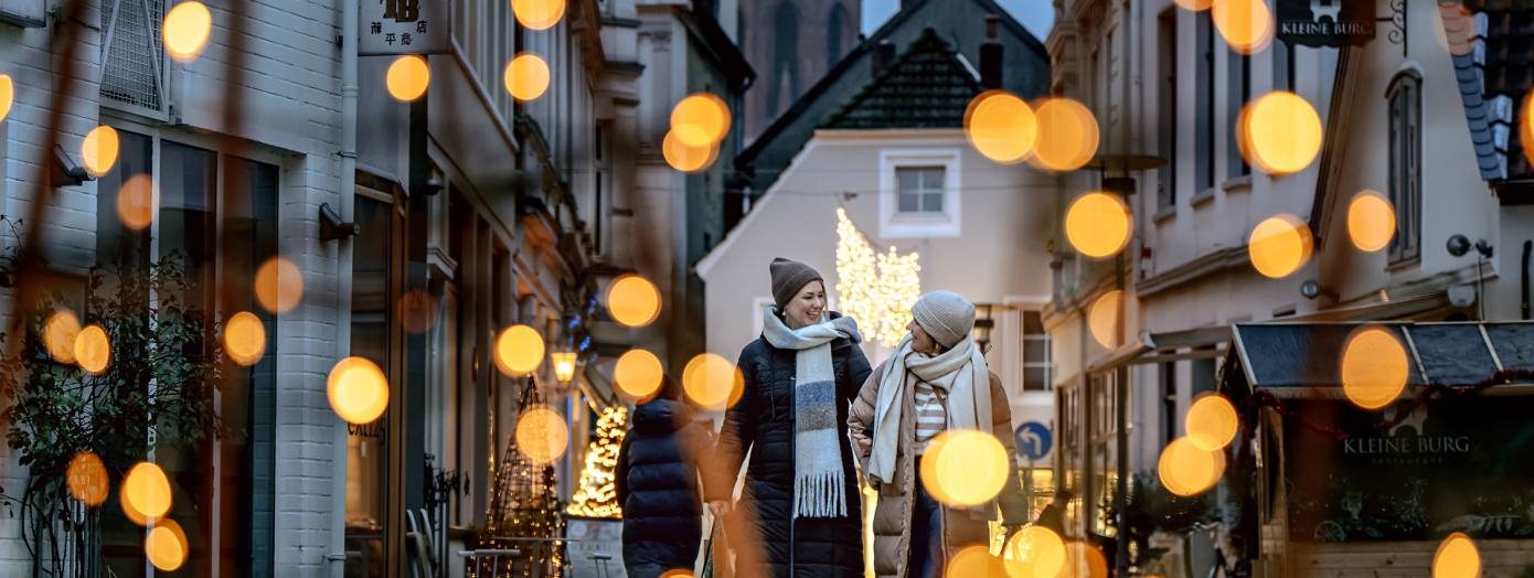 Zwei Frauen gehen durch die weihnachtlich beleuchtete Burgstraße in Oldenburg. 