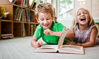 Zwei Kinder liegen auf dem Boden und lesen auf der Kinder- und Jugendbuchmesse ein Buch.