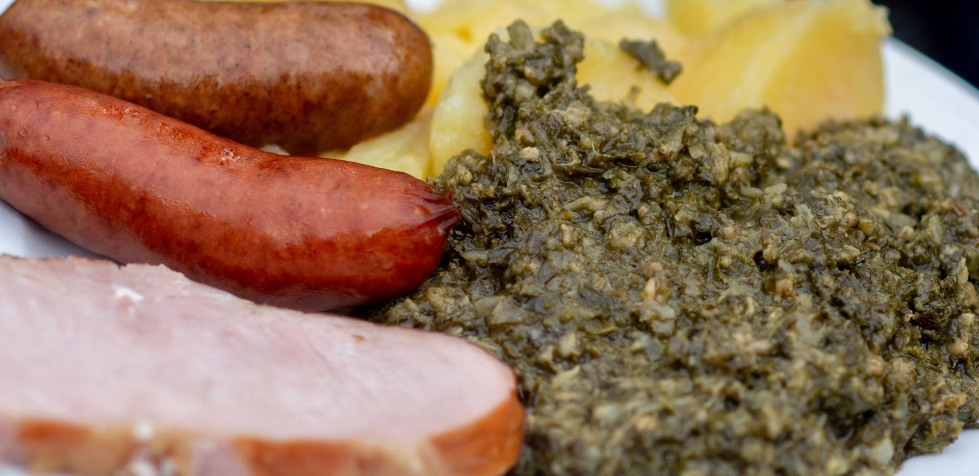 Grünkohl mit Salzkartoffeln, Pinkelwurst und Kassler auf einem Teller. 