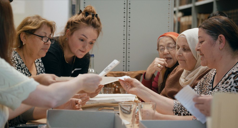 Ältere Frauen sitzen an einem Tisch und schauen sich Briefe an.