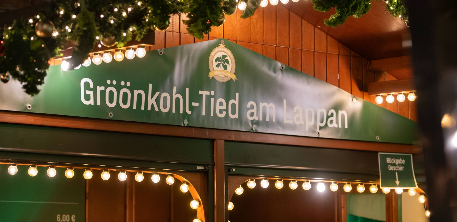 Schild an der Holzbude "Gröönkohl-Tied am Lappan" und Weihnachtsschmuck. Schild an der Holzbude