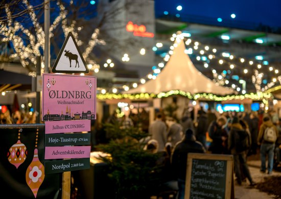 Schild Skandinavisches Weihnachtsdorf Oldenburg mit beleuchtetem Markt im Hintergrund