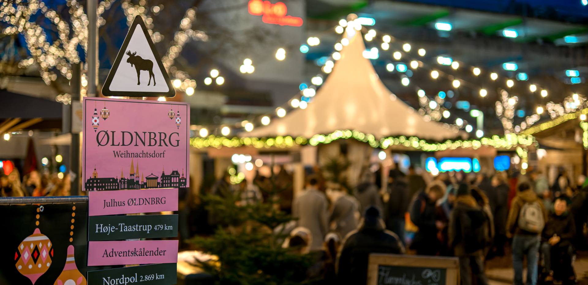 Skandinavisches Weihnachtsdorf Oldenburg Schild Skandinavisches Weihnachtsdorf Oldenburg mit beleuchtetem Markt im Hintergrund