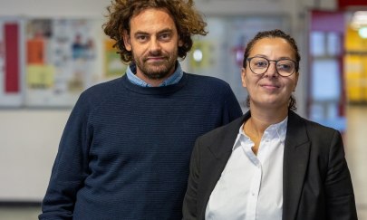 Brustbild von Shai Hoffmann und Jouanna Hassoun in frontaler Sicht. Beide stehen in einem Schulflur. Der Hintergrund ist unscharf, erkennbar sind - vermutlich von Schülerinnen angefertigte - Wandzeitungen an der Flurwand. Brustbild von Shai Hoffmann und Jouanna Hassoun in frontaler Sicht. Beide stehen in einem Schulflur. Der Hintergrund ist unscharf, erkennbar sind - vermutlich von Schülerinnen angefertigte - Wandzeitungen an der Flurwand.